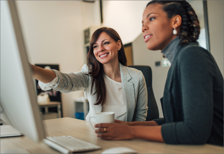 one woman pointing at a computer screen sitting next to another woman