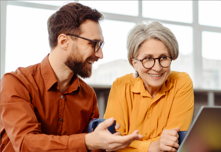 two people holding cups talking and looking at laptop